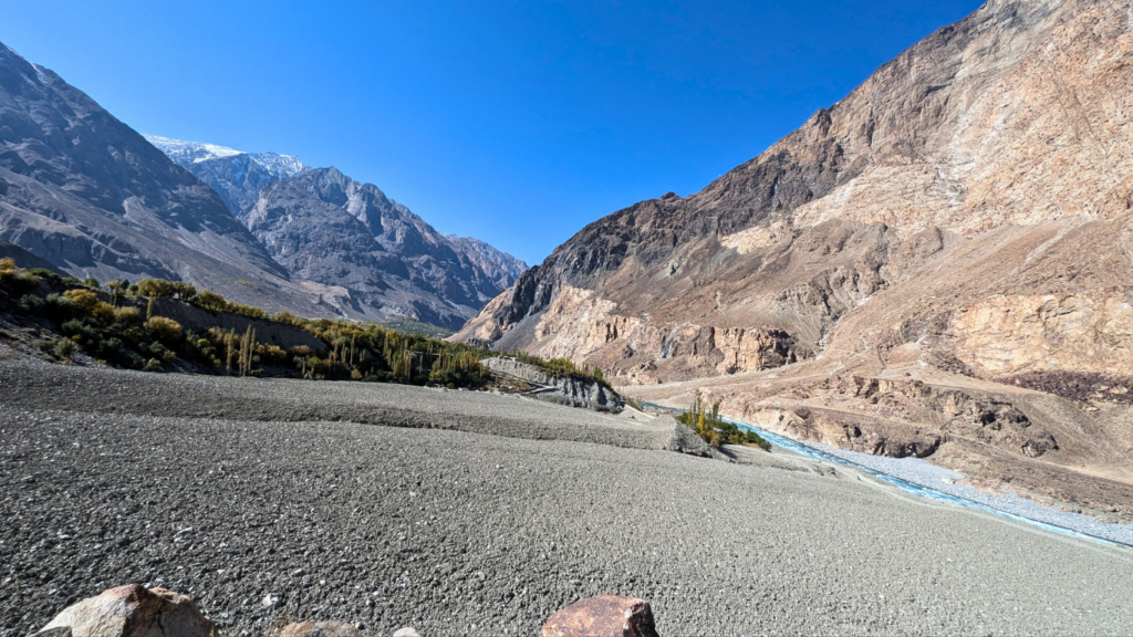 Rocky river valley in Talidass, Ghizer District after the August 2025 GLOF, showing a buried village, debris-covered floodplain, and barren mountain slopes under a clear blue sky.