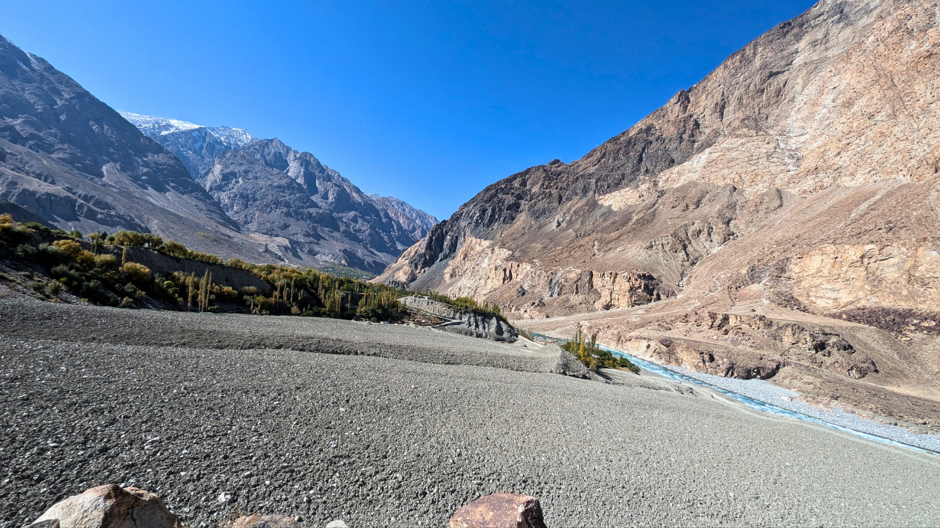Rocky river valley in Talidass, Ghizer District after the August 2025 GLOF, showing a buried village, debris-covered floodplain, and barren mountain slopes under a clear blue sky.